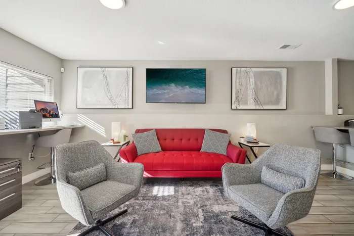 ReNew Foothills Bright living area with a red sofa, two gray chairs, and modern decor, featuring art and a wall-mounted screen.