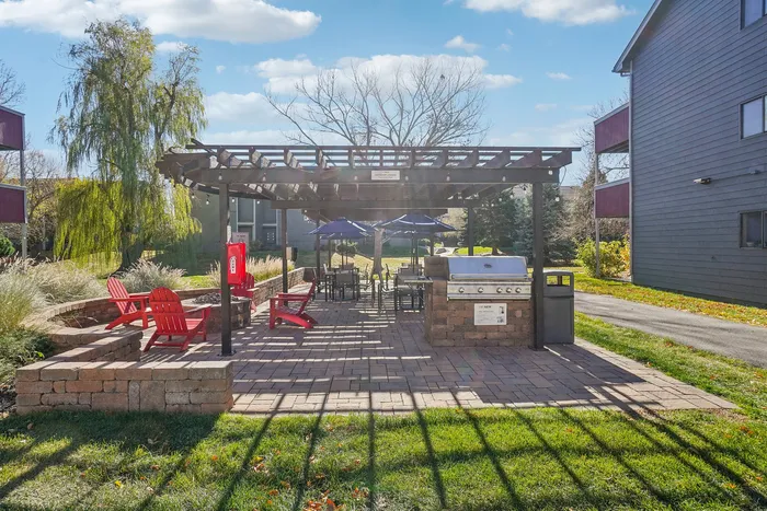 ReNew Foothills Inviting patio space with red Adirondack chairs, outdoor grill, and pergola under a clear sky.
