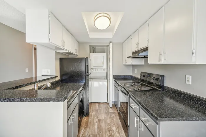ReNew Foothills Bright and sleek kitchen with black countertops, white cabinetry, and modern appliances, featuring a stacked washer and dryer.