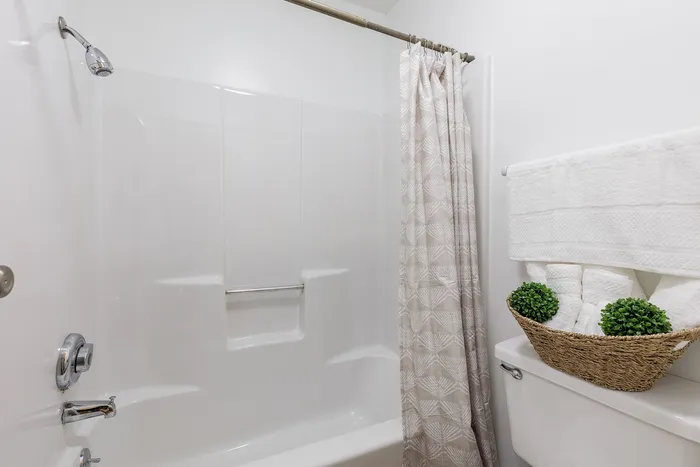 Chic bathroom featuring a sleek white bathtub, a stylish shower curtain, and carefully arranged towels in a decorative basket.