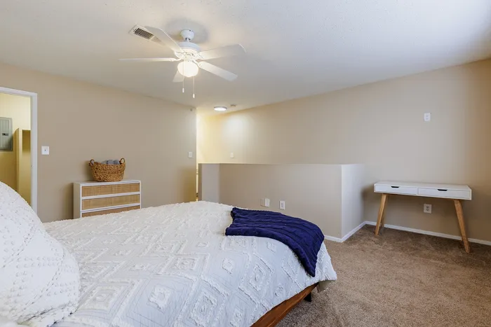 Inviting bedroom with stylish decor, featuring a comfortable bed, soft carpet, and a ceiling fan.