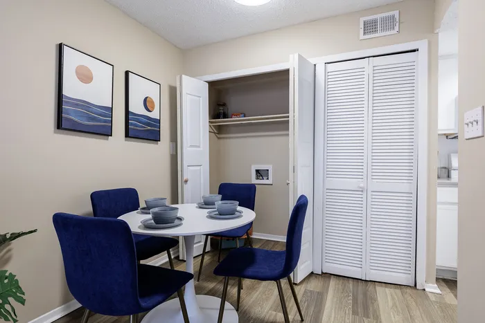 Modern dining area with blue velvet chairs and minimalist art on beige walls.