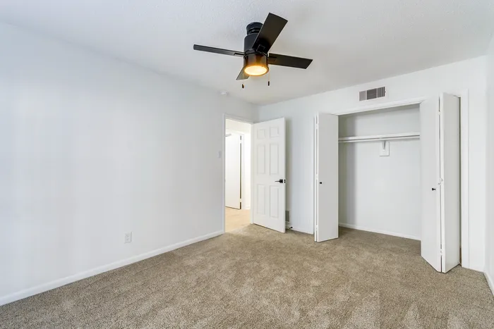 Bright and modern bedroom at ReNew on Cantrell with plush carpet, featuring a ceiling fan and spacious closet for ultimate comfort and convenience.