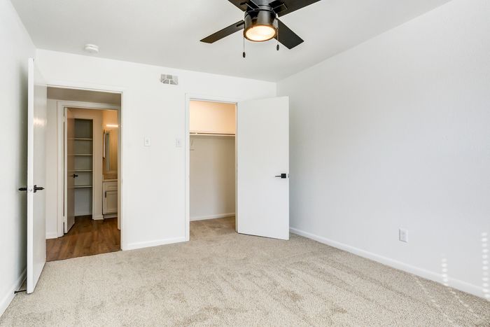 Bright, inviting bedroom at ReNew on Cantrell with plush carpeting, ceiling fan, and a spacious walk-in closet, perfect for comfort and organization.