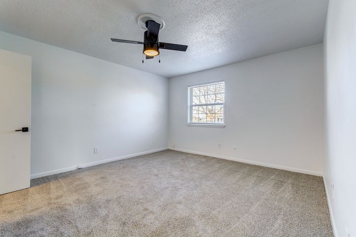 Bright and inviting bedroom at ReNew on Cantrell with modern ceiling fan, plush carpeting, and a sunny window providing natural light.