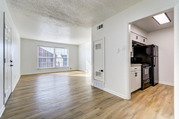 Bright and airy living area at ReNew on Cantrell with elegant wood flooring and a modern kitchen, featuring large windows that illuminate the space.