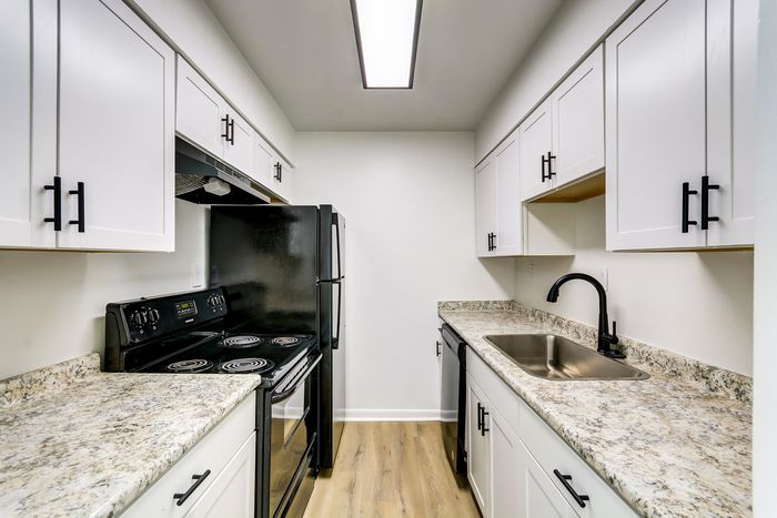 Modern kitchen at ReNew on Cantrell featuring sleek black appliances, elegant white cabinetry, and granite countertops.