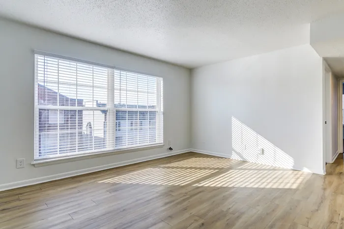 Bright and spacious living area at ReNew on Cantrell featuring large windows with elegant blinds, showcasing sleek hardwood floors and abundant natural light.