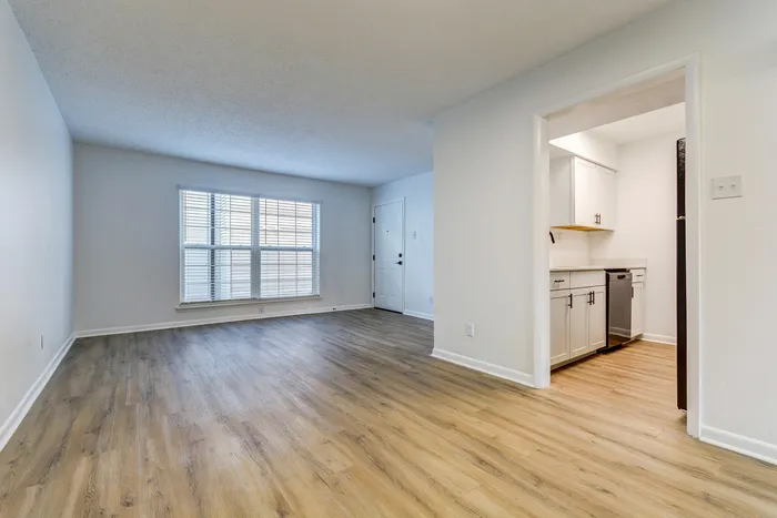 Spacious living room at ReNew on Cantrell with modern wood flooring and large windows leading into a sleek, contemporary kitchen.