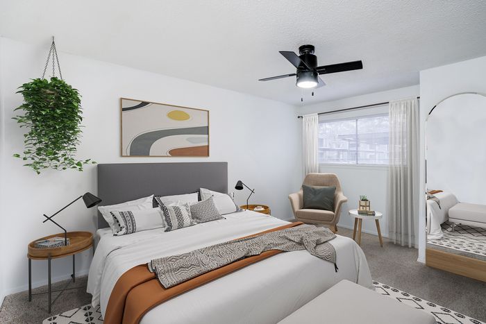 Chic and modern bedroom with stylish decor and cozy seating, enhanced by natural light and a lush hanging plant.