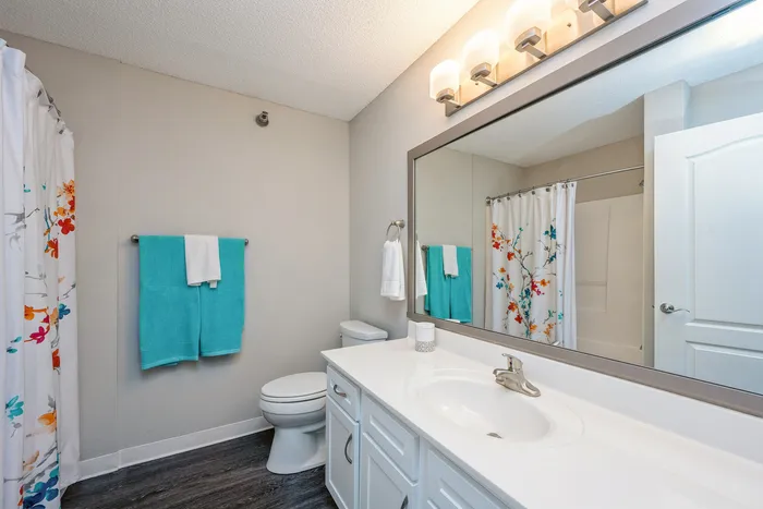 Bright and modern bathroom with floral shower curtain, elegant vanity, and vibrant turquoise towels.