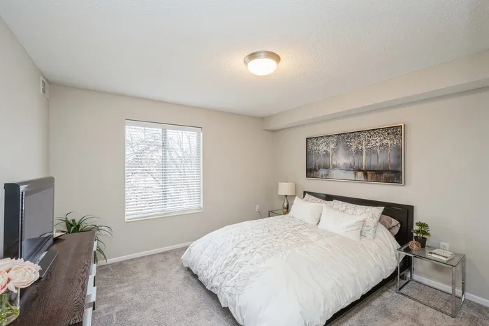 Inviting bedroom with cozy carpeting, a warm neutral palette, and large window offering natural light.