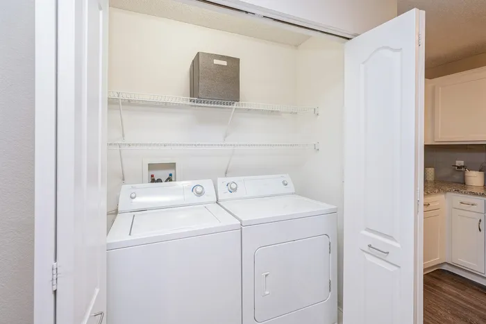 Bright utility room with modern washer and dryer, complemented by practical shelving and adjacent to a stylish kitchen.