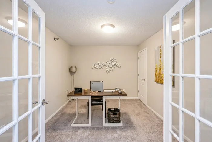 Chic home office with elegant French doors, plush carpeting, and tasteful wall art, creating a perfect work-from-home environment.