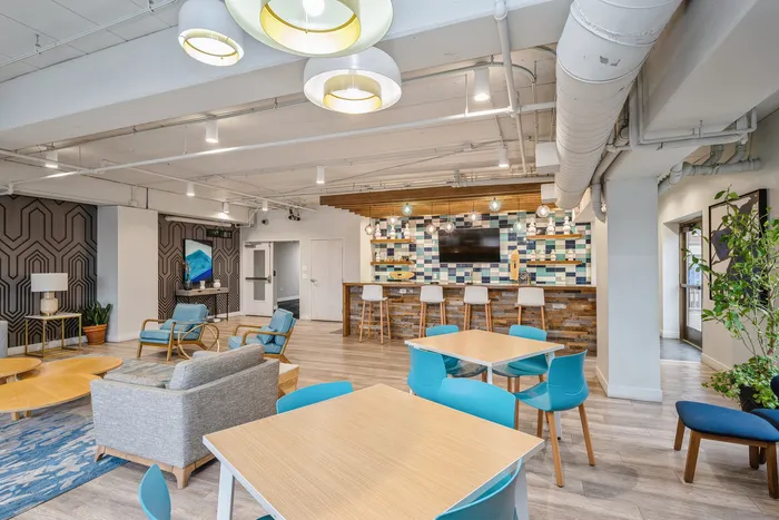 Modern communal space featuring vibrant seating, stylish decor, and a chic bar area with colorful tile backsplash.
