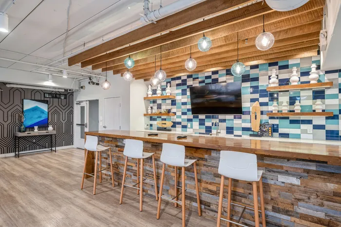 Modern communal space with stylish bar seating, vibrant tiled backsplash, and chic pendant lights, ideal for social gatherings.