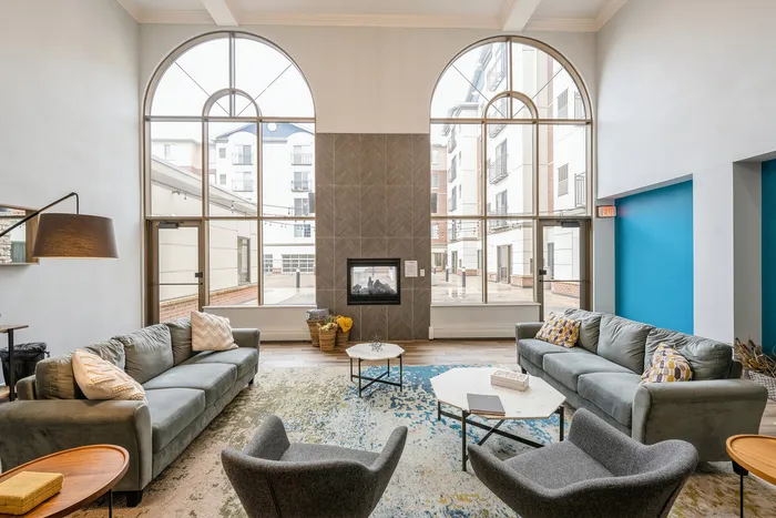 Elegant apartment lounge with high ceilings, large arched windows, cozy seating, and modern fireplace.