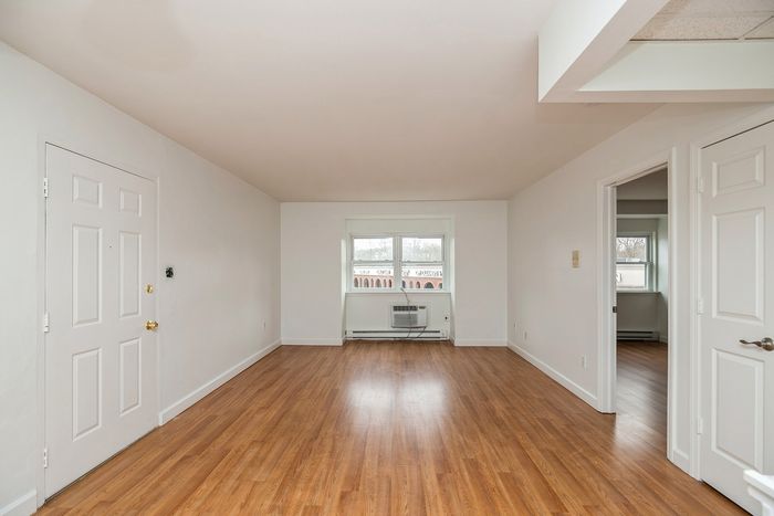 Bright and spacious living room with elegant hardwood flooring, large window, and fresh white walls creating a welcoming atmosphere.