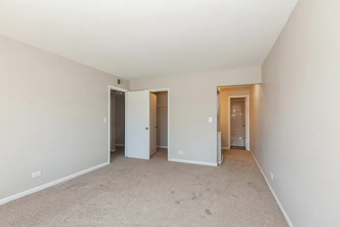 Spacious bedroom with plush carpet, neutral walls, and ample natural light. Features include a cozy walk-in closet and an adjacent modern bathroom.