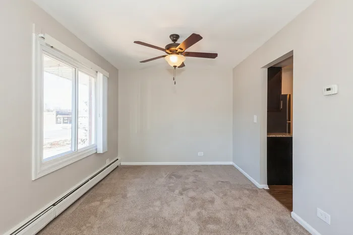 Bright, sunlit room with a plush carpet and stylish ceiling fan, offering a cozy, inviting atmosphere perfect for relaxation.