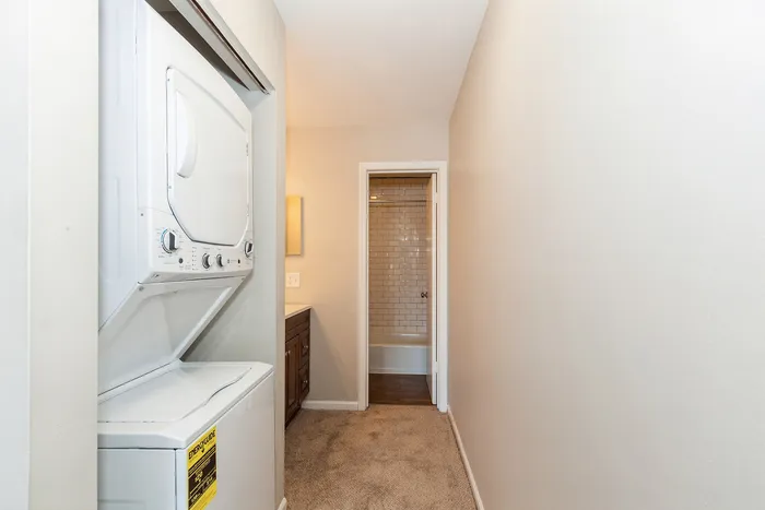 Convenient apartment hallway featuring an in-unit washer and dryer next to a modern bathroom with sleek tile details.