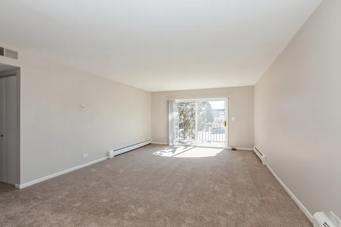 Bright and inviting living room with plush carpeting and large sliding glass doors leading to a scenic balcony view.