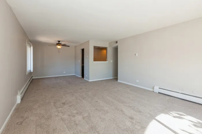 Spacious living room with plush carpeting, bright natural light, and modern ceiling fan, perfect for cozy gatherings.