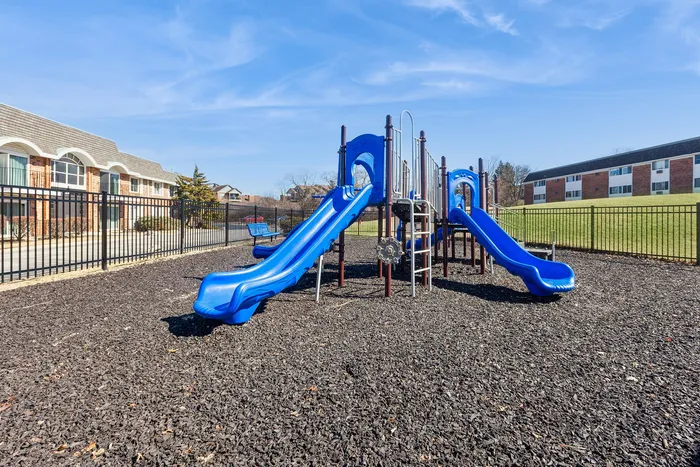 Inviting playground with vibrant blue slides and climbing structure, nestled in a picturesque residential community.