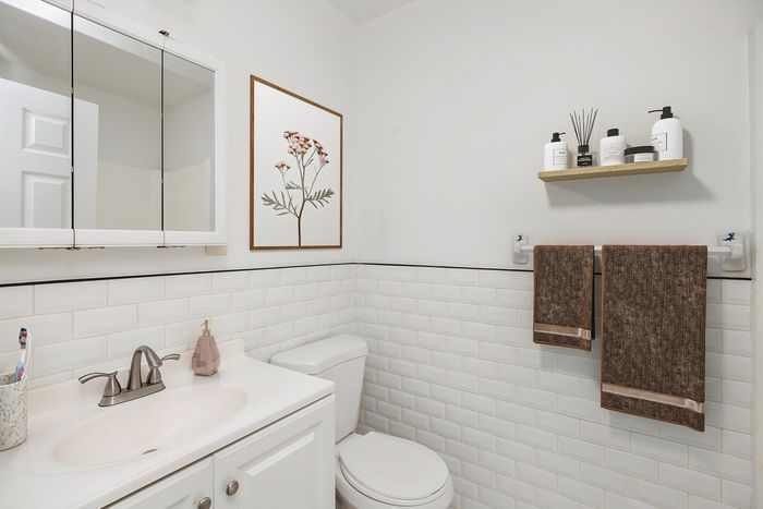 Chic white bathroom featuring a modern vanity, elegant floral artwork, and stylish wall-mounted toiletries.