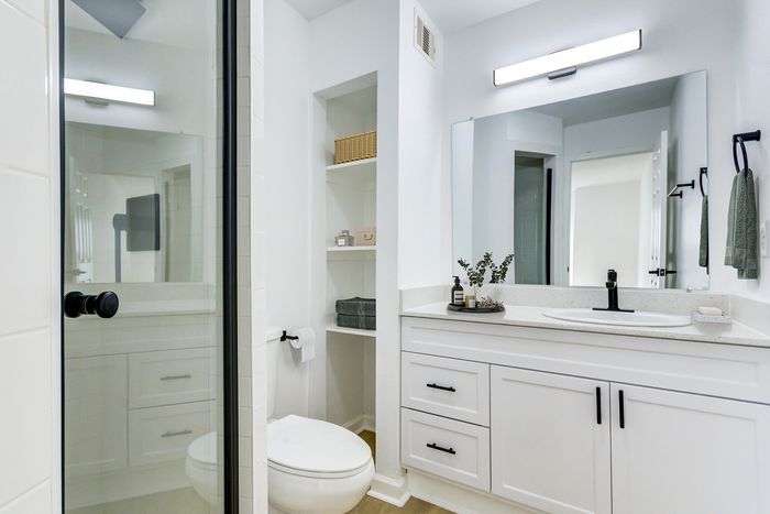 Bright and modern bathroom at ReNew on Cantrell featuring sleek white cabinetry, spacious mirror, and elegantly styled open shelving.