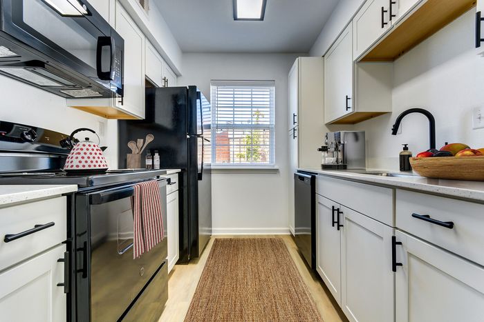 Modern, well-lit kitchen at ReNew on Cantrell with sleek black appliances, white cabinetry, and a cozy rug, perfect for culinary creativity.