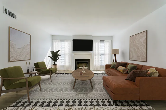 Contemporary living room at ReNew on Cantrell featuring a stylish leather sofa, chic green armchairs, and a cozy fireplace beneath a sleek TV.