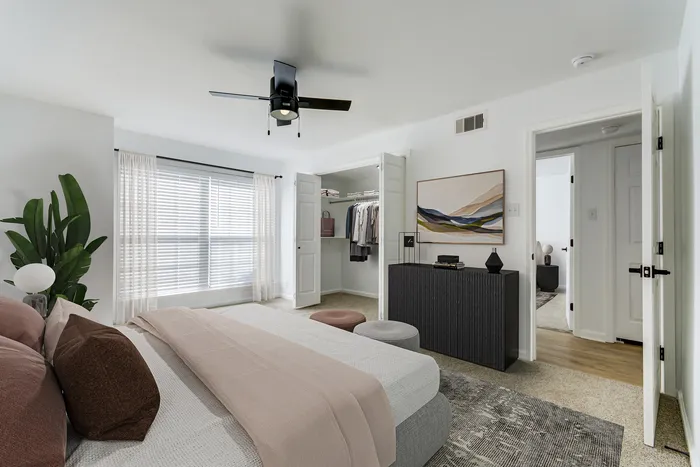 Elegant bedroom at ReNew on Cantrell with chic decor, featuring a sleek ceiling fan, open closet, and large window with sheer curtains for abundant natural light.