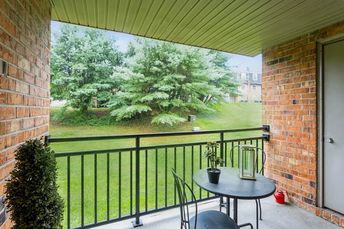 Charming balcony at ReNew Howard Crossing  with brick walls overlooking lush green landscape, featuring a cozy outdoor table for perfect relaxation.