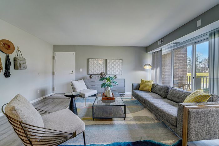 Chic living room at ReNew White Marsh with cozy grey furniture, accent pillows, stylish decor, and sunlit balcony view.