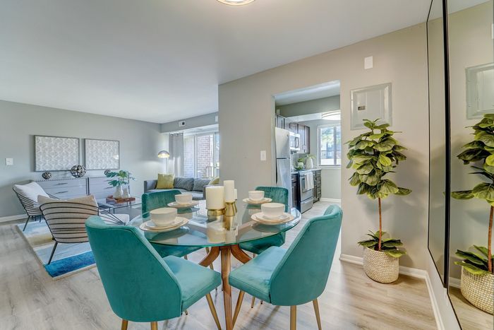 Chic apartment interior at ReNew White Marsh featuring a modern dining area with teal chairs, elegant table settings, and a cozy living space with stylish decor and natural lighting.