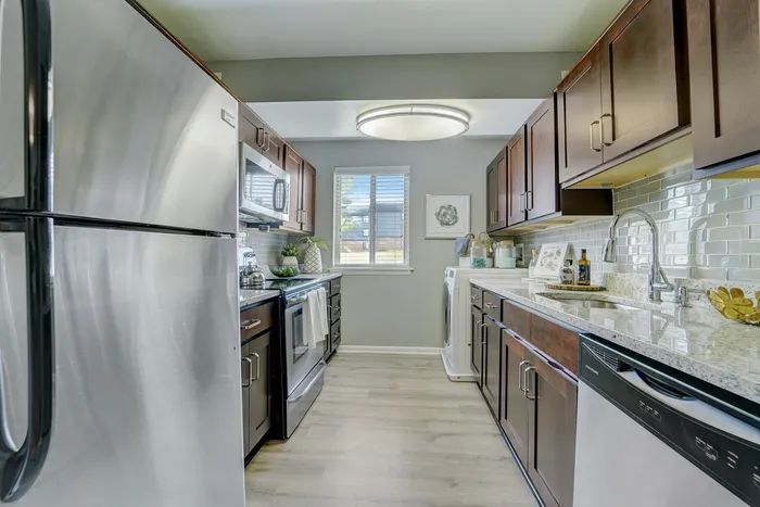 Modern galley kitchen at ReNew White Marsh with sleek stainless steel appliances, elegant wooden cabinets, and chic subway tile backsplash.