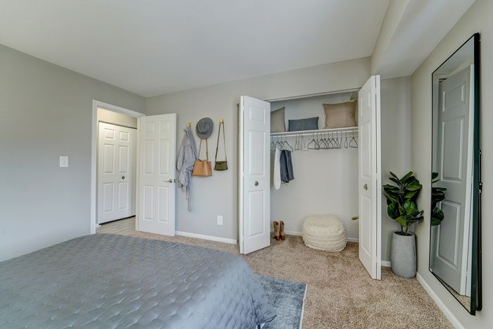 Inviting bedroom at ReNew White Marsh with plush gray bedding, walk-in closet, and modern decor featuring a tall mirror and indoor plant.