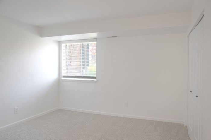 Bright and inviting empty room at ReNew White Marsh with soft carpet flooring, large window for natural light, and classic white walls offering a blank canvas for your personal touch.