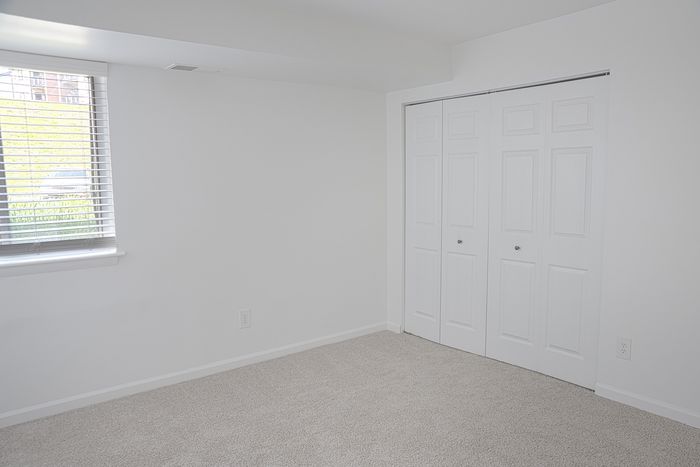 Bright and airy bedroom at ReNew White Marsh with plush carpeting, large window offering natural light, and spacious white closet doors.