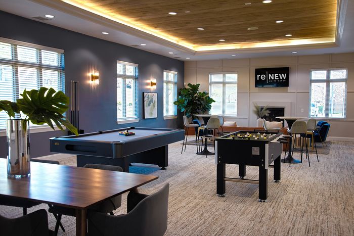 Luxurious game room featuring a sleek billiards table, foosball, and plush seating in a sunlit, modern apartment community.