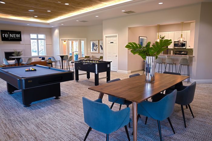 Modern community lounge featuring pool and foosball tables, a stylish dining area, and a sleek kitchen with bar seating, perfect for social gatherings.