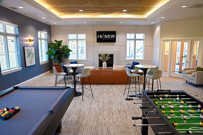 Chic community lounge featuring a cozy fireplace, stylish seating, and games like pool and foosball, perfect for relaxation and socializing.