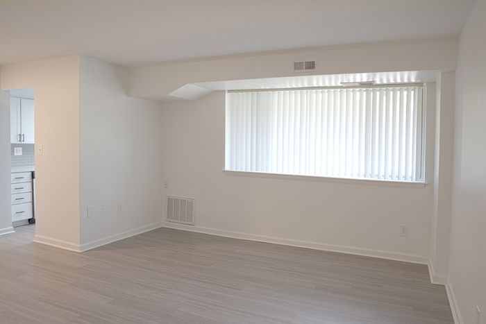 Bright and inviting living space at ReNew White Marsh with large window, sleek laminate flooring, and open access to a modern kitchen.