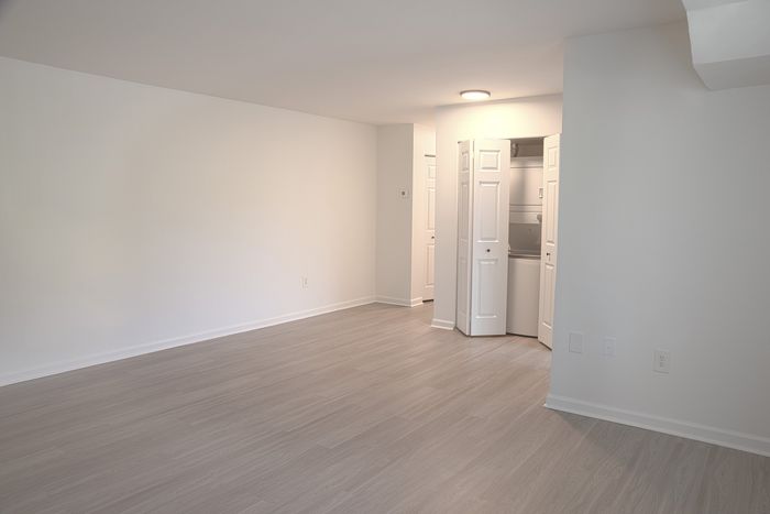 Modern open space at ReNew White Marsh with sleek wood flooring, bright white walls, and convenient in-unit laundry closet.