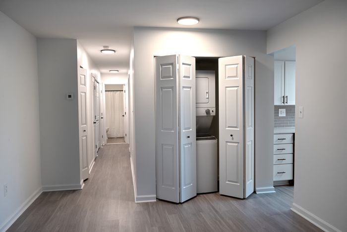 Modern hallway at ReNew White Marsh featuring elegant wood flooring, built-in laundry area with chic sliding doors, and streamlined kitchen entry with sleek cabinetry.