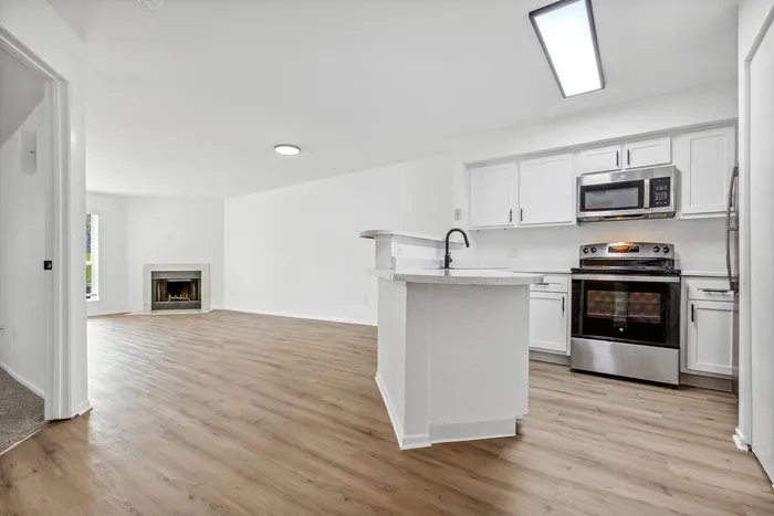 Modern open-concept living space featuring sleek hardwood floors, a cozy fireplace, and a contemporary kitchen with stainless steel appliances.