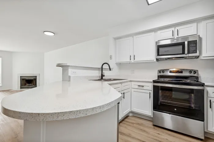 Modern kitchen with sleek appliances, spacious countertops, and open layout extending to a cozy living area with a fireplace.