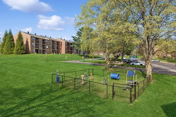 Charming apartment complex at ReNew Howard Crossing with spacious green lawns and a quaint fenced playground area, perfect for outdoor enjoyment.
