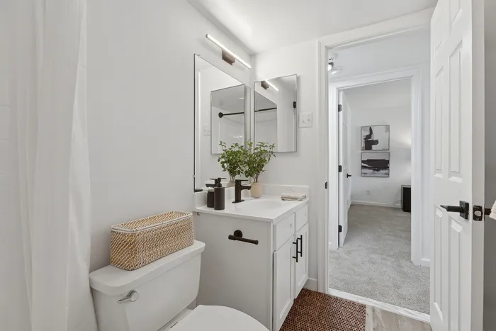 Bright and modern bathroom at ReNew Howard Crossing featuring sleek white cabinetry, elegant fixtures, and a stylish plant accent, seamlessly connected to a cozy adjacent room.